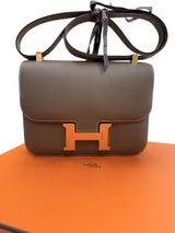 Hermès Constance 24 Brown Epsom Leather Crossbody Shoulder Bag displayed on an orange surface.