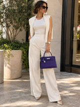 Model carrying the Hermès Kelly Sellier 25 purple Epsom leather handbag with palladium hardware in a cream outfit.