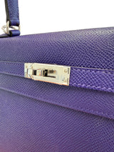 Close-up of a purple pebbled leather handbag with a silver-toned metal lock and strap attachment on a white background.