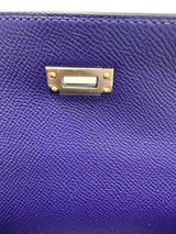 Close-up of a purple textured leather item featuring a rectangular gold-tone metal clasp with four gold rivets.
